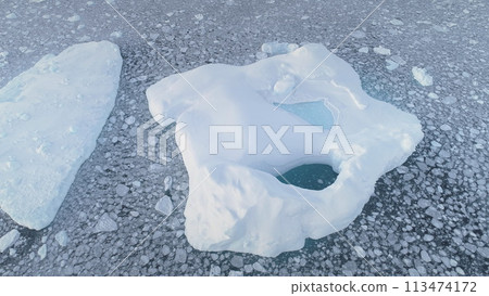 Aerial of close-up iceberg with pool. Antarctica zoom in drone flight. Ice mountain among polar ocean. Pieces of ice floating around frozen icebergs. Permafrost. Antarctic continent. 113474172