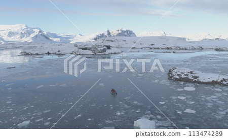 People in rubber inflatable motor boat sail in Antarctic ice to Akademik Vernadsky polar station. Tracking Aerial View. Expedition Transport Exploring Extreme Cold Water. Drone 113474289
