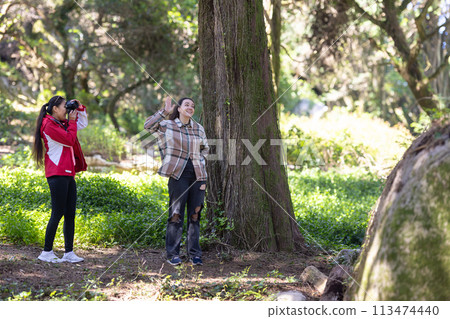 Two young Women Standing Next to a Tree 113474440