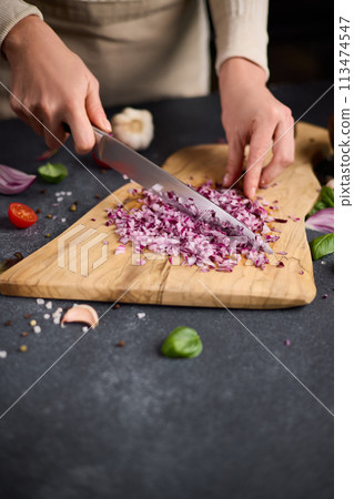 Woman chopping red Mars onion on wooden cutting board at domestic kitchen Woman chopping red Mars onion on wooden cutting board at domestic kitchen 113474547