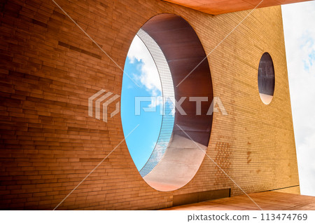 Futuristic geometric abstraction perspective in the form of a wall with rectangular tiles and two holes in the wall, one of them can see a blue sky with clouds. Horizontal photo 113474769