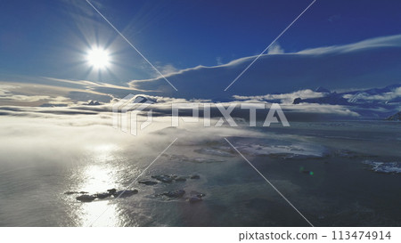 Antarctica landscape. Aerial view drone flight. Sun track of white bright polar sun over the ocean covered by light fog. Ice and snow covered surface of Antarctic continent. Panoramic overview. 113474914