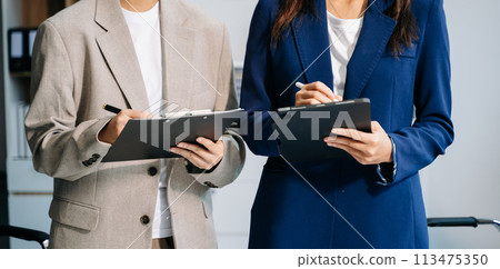 Business documents on office table with smart phone and laptop and two colleagues discussing data in the background .. 113475350