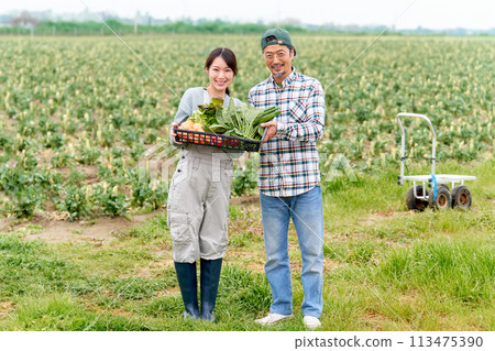 A young woman and a veteran farmer smiling while carrying crops 113475390