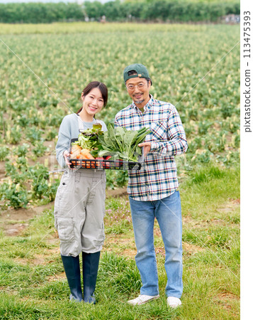 一位年輕女子和一位經驗豐富的農民拿著農作物微笑。 113475393