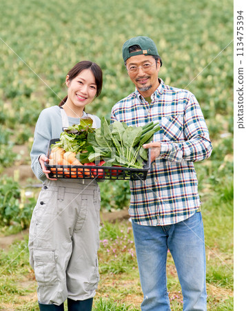一位年輕女子和一位經驗豐富的農民拿著農作物微笑。 一位年輕女子和一位經驗豐富的農民拿著農作物微笑。 113475394