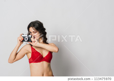 Beautiful female with pretty smile in red lingerie holding photo camera, isolated on white 113475970