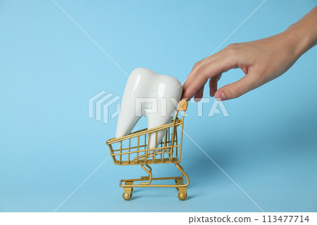 Tooth in shopping cart and hand on blue background 113477714