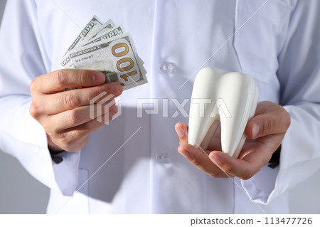Dollars and tooth in hands of dentist on gray background Dollars and tooth in hands of dentist on gray background 113477726