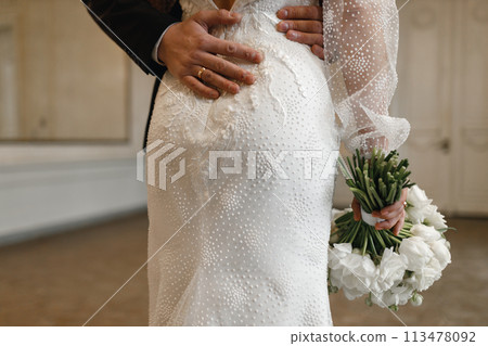The groom hugs the bride in a wedding dress with a bouquet in his hand 113478092