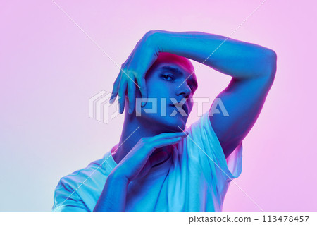 Portrait of young man with bald head posing in white casual t-shirt on gradient blue pink background in neon light 113478457