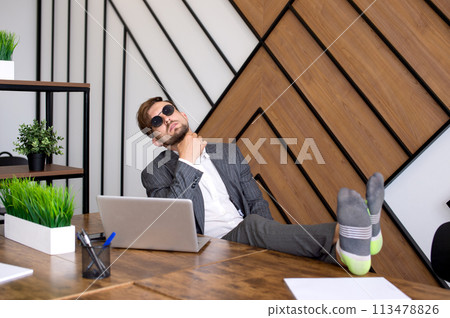 A man is sitting in the office with a laptop, his feet are on the table. Procrastinating A man is sitting in the office with a laptop, his feet are on the table. Procrastinating 113478826