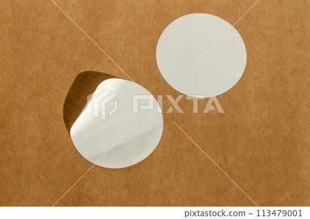 Round white stickers on brown paper background with natural sunlight. 113479001