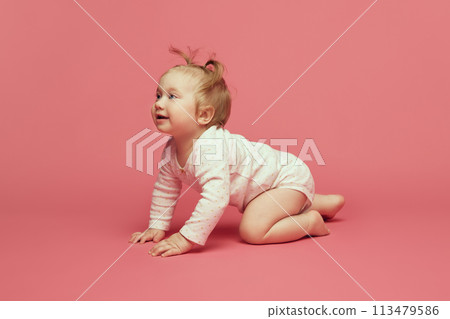 Smiling happy little baby girl, toddler in comfortable onesie crawling, playing on pink background. Joyful time Smiling happy little baby girl, toddler in comfortable onesie crawling, playing on pink background. Joyful time 113479586