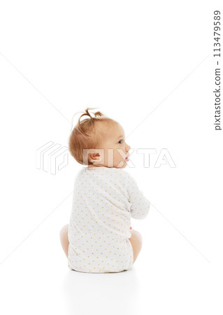Cute little baby girl sitting in comfortable clothes and looking with curiosity isolated on white background. Careless happy kid 113479589