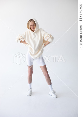 Beautiful blonde woman posing in white hoodie and leggings posing against white background 113479700
