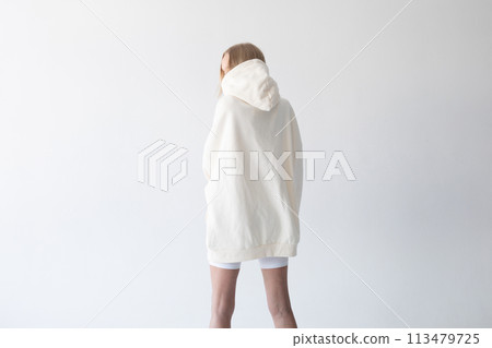 Beautiful blonde woman posing in white hoodie and leggings posing against white background. Posing with his back. 113479725