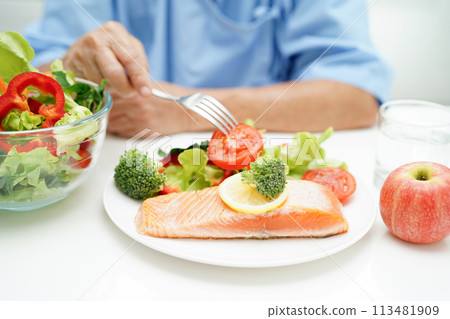 Asian elderly woman patient eating salmon stake and vegetable salad for healthy food in hospital. Asian elderly woman patient eating salmon stake and vegetable salad for healthy food in hospital. 113481909