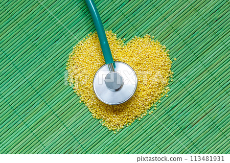 Millet groats heart shaped on green mat surface. 113481931