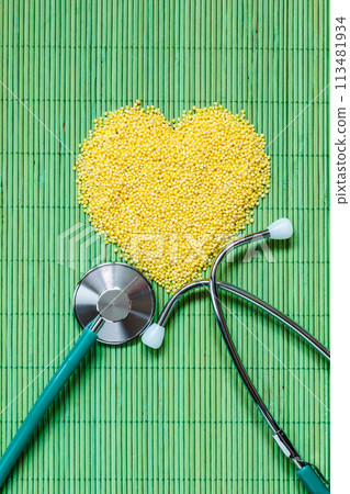 Millet groats heart shaped on green mat surface. Millet groats heart shaped on green mat surface. 113481934