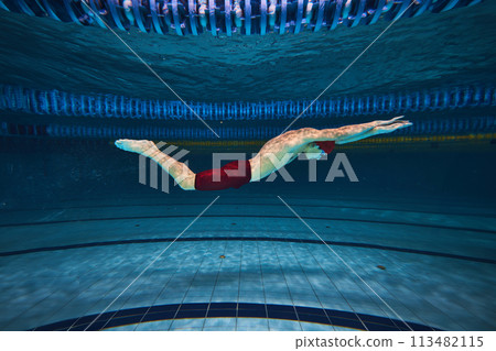 Butterfly swim style. Athletic young man, swimmer in motion training, preparing for competition, swimming in pool indoors. 113482115