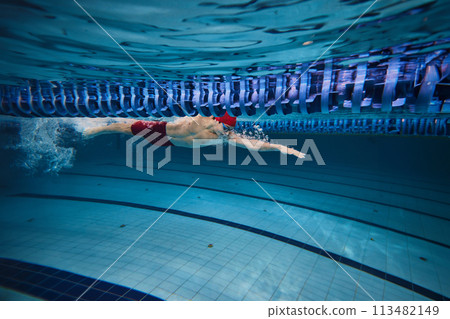 Power, concentration and resilience. Young athletic man, swimmer in motion, swimming freestyle in pool indoors, training 113482149