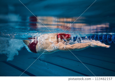 Muscular young man, swimmer in motion, preparing for competition, training in swimming pool indoors. Speed and technique 113482157