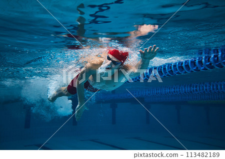 Athletic grace and strength. Young man in cap and goggles, swimmer in motion underwater training in swimming pool 113482189