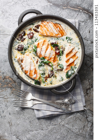 Tuscan grilled salmon in creamy sauce with spinach, sun dried tomatoes and parmesan closeup in the pan. Vertical top view Tuscan grilled salmon in creamy sauce with spinach, sun dried tomatoes and parmesan closeup in the pan. Vertical top view 113483891