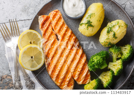 Grilled salmon, boiled potatoes, broccoli and cream sauce in a plate. Horizontal top view 113483917