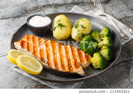 Dietary grilled salmon with boiled potatoes, broccoli, lemon, herbs and cream sauce close-up in a plate. Horizontal Dietary grilled salmon with boiled potatoes, broccoli, lemon, herbs and cream sauce close-up in a plate. Horizontal 113483922