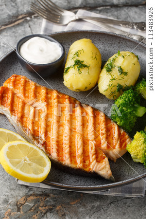 Grilled salmon steak with new potatoes, broccoli and cream sauce close-up in a plate. Vertical 113483926