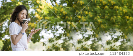 Banner Woman use smartphone drinking coffee hand holding hot disposable cup in green park. Web Banner Happy Relax asian woman smiling face at outdoors garden. Young women enjoy nature with copy space 113484353
