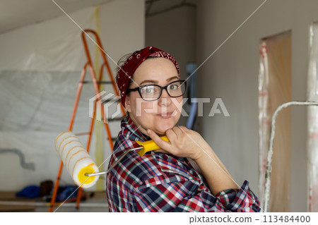 Smiling woman in glasses with a roller in hands is preparing for painting work 113484400