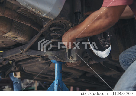 Close up Man hands fixing Shock absorber machinery vehicle mechanical service. Mechanic man hands repairing car auto repair shop uses jack change tyre. Vehicle Car overhaul maintenance engineer 113484709