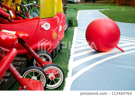 Colorful playground equipment with red toy cars and a ball on artificial turf 113484764