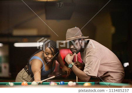 Portrait of adult African American couple playing pool together and leaning over table in nightclub 113485237