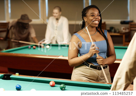 Waist up portrait of smiling African American woman chatting with friend while enjoying game of pool together in low light copy space Waist up portrait of smiling African American woman chatting with friend while enjoying game of pool together in low light copy space 113485257