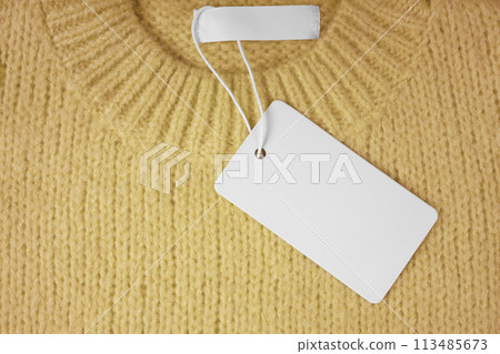 Blank clothing tag and inner label on neck of yellow knitted sweater background 113485673