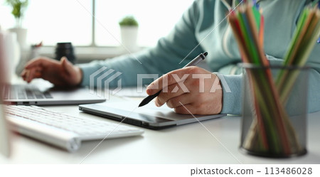 A young designer holds a pen from a tablet in his 113486028