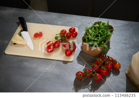 Top view of fresh organic ingredients for a healthy salad. Eco-friendly cardboard box with arugula leaves, a bunch of red ripe cherry tomatoes and a slice of parmesan cheese on a cutting board. Top view of fresh organic ingredients for a healthy salad. Eco-friendly cardboard box with arugula leaves, a bunch of red ripe cherry tomatoes and a slice of parmesan cheese on a cutting board. 113486235