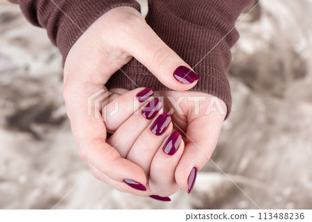 A woman in a brown jacket with a blackberry-colored manicure. 113488236