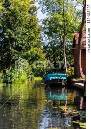 Scenic view green riverside garden house moored boat  german national biosphere reserve park Spreewald spring summer sunny day. Spree river forest greenery canal nature tranquil landscape in Germany 113488495