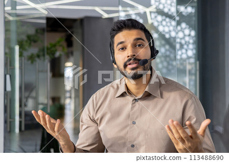 An engaging Indian businessman communicates while wearing a headset, showcasing his professional demeanor and expert communication skills in a stylish office setting. 113488690