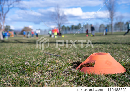 Selective focus on a soccer practice field cone on grass with blurred kids in the background 113488831