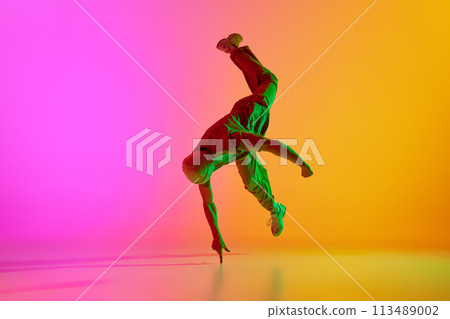Dynamic photo of young, talented man dancing in freestyle in neon light against gradient pink-yellow background. 113489002