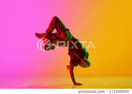 Dynamic photo of young, talented man dancing breakdance moves in neon light against gradient pink-yellow background. Dynamic photo of young, talented man dancing breakdance moves in neon light against gradient pink-yellow background. 113489004