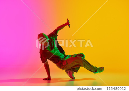 Talented dancer dressed streetwear performing freestyle moves in motion in neon light against gradient pink-yellow background. 113489012