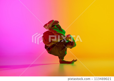 Talented freestyle dancer, young man stands in freeze in neon light against gradient pink-yellow background. Talented freestyle dancer, young man stands in freeze in neon light against gradient pink-yellow background. 113489021