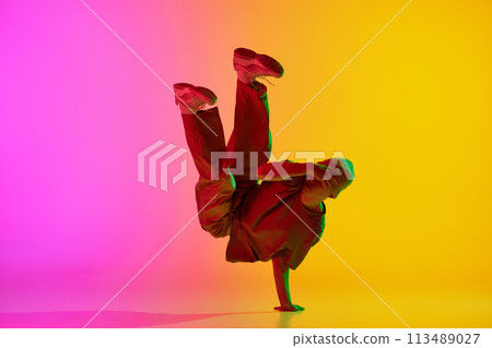 Artistic, young man, break-dancer dancing in motion in neon light against gradient pink-yellow background. Artistic, young man, break-dancer dancing in motion in neon light against gradient pink-yellow background. 113489027